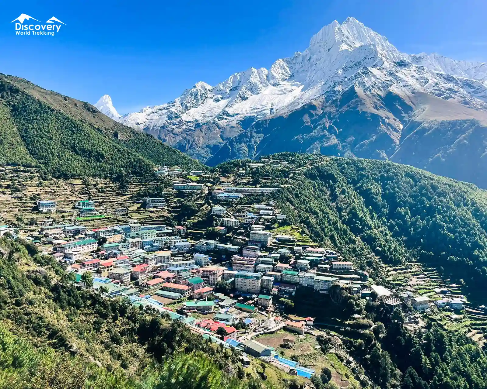 The vibrant Sherpa town of Namche Bazaar. In the distance, Mount Everest peeks above the ridges, surrounded by other Himalayan peaks.