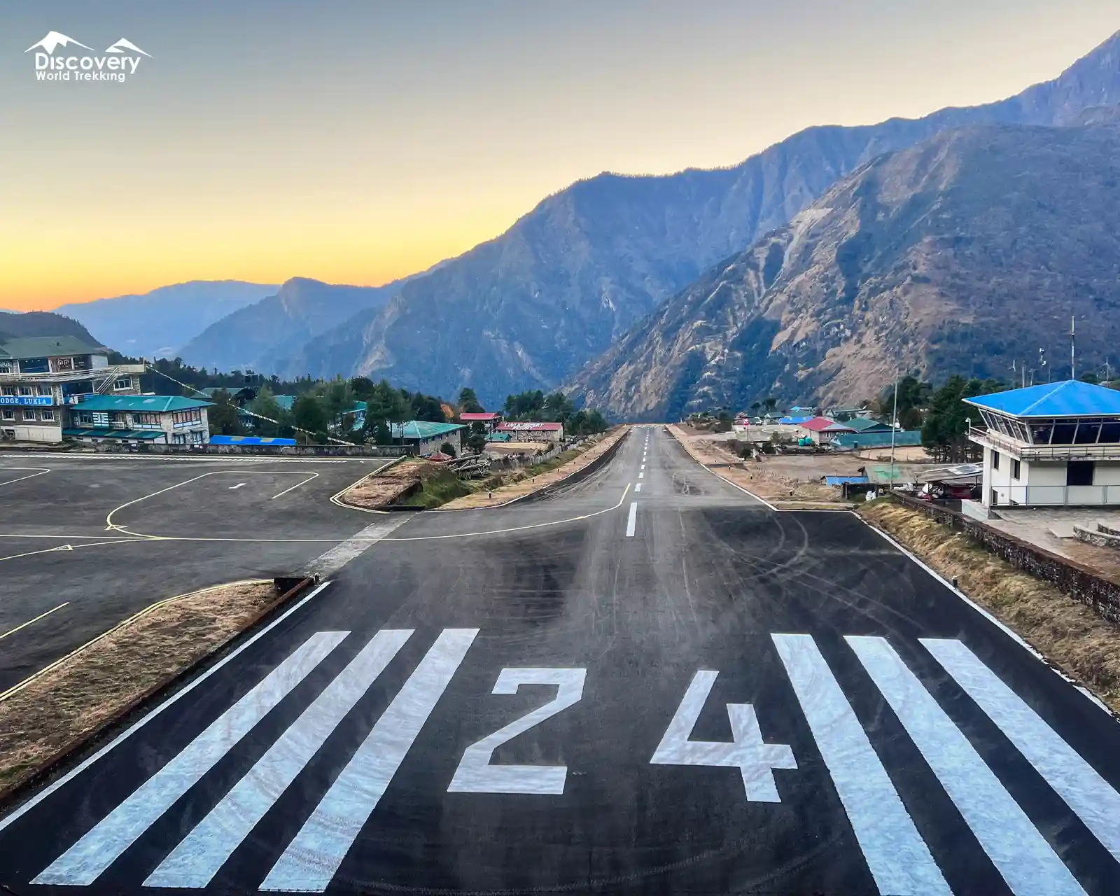 Steep runway of Tenzing-Hillary Airport, the gateway to Everest Region, surrounded by mountains and small buildings at sunrise or sunset.